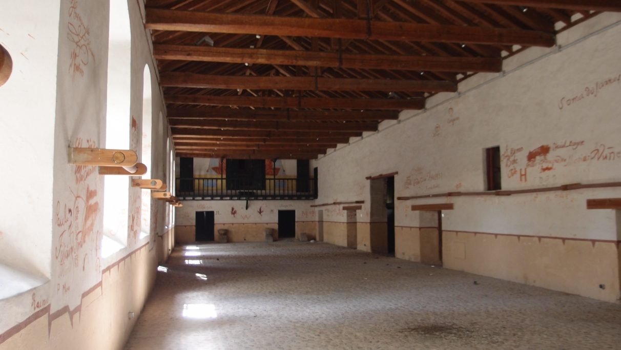 Interior de un amplio salón con techo de madera y paredes blancas. Sin mobiliario visible.