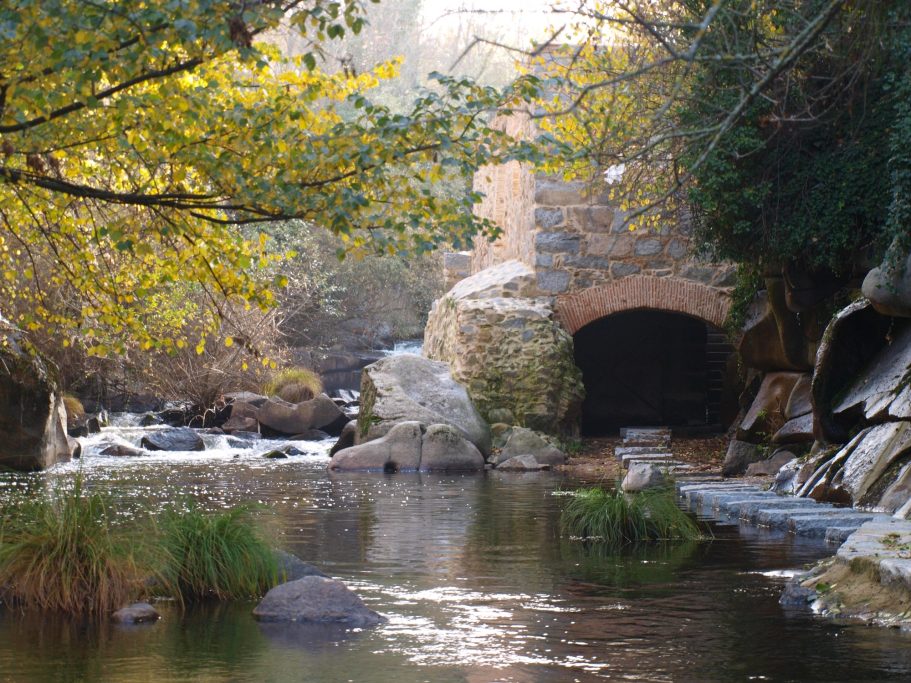 Río sereno con un puente de piedra y vegetación verde a su alrededor.