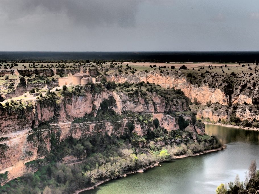 Vista de un acantilado sobre un río, con vegetación y cielo nublado en el horizonte.