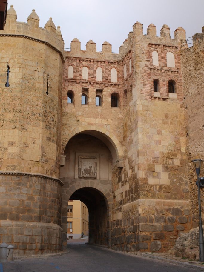 Puerta de una antigua muralla con torres y arcos en un entorno histórico.