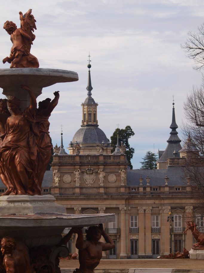 Fuente ornamental en primer plano con un palacio de fondo bajo un cielo nublado.