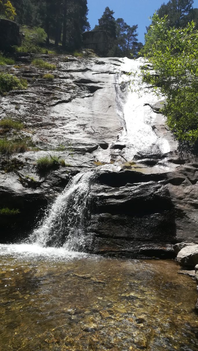 Cascada sobre rocas, con agua fluyendo y vegetación en los alrededores.