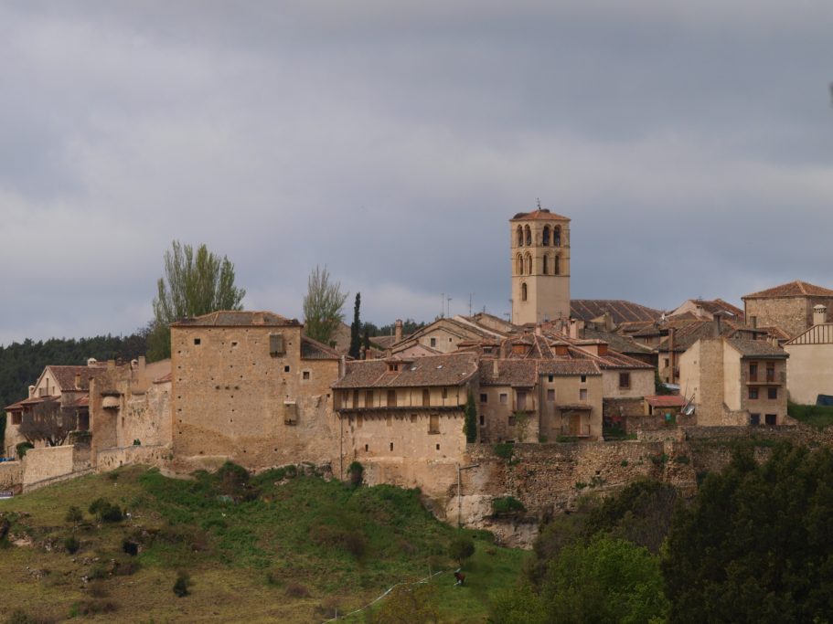 Vista de un pueblo rural con casas de piedra y una torre en el horizonte.
